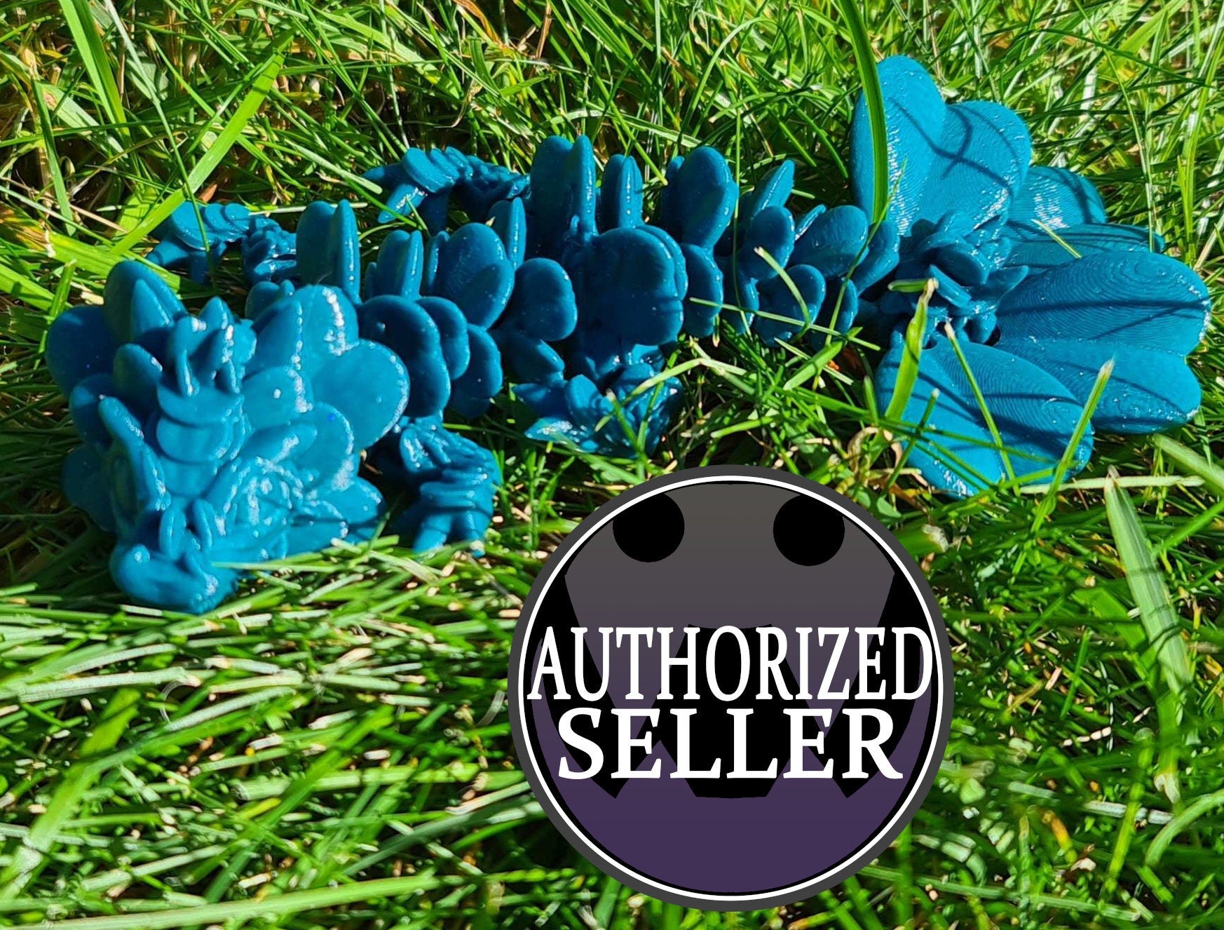 Blue 3D printed dragon toy on green grass with a round 'Authorized Seller' badge in front