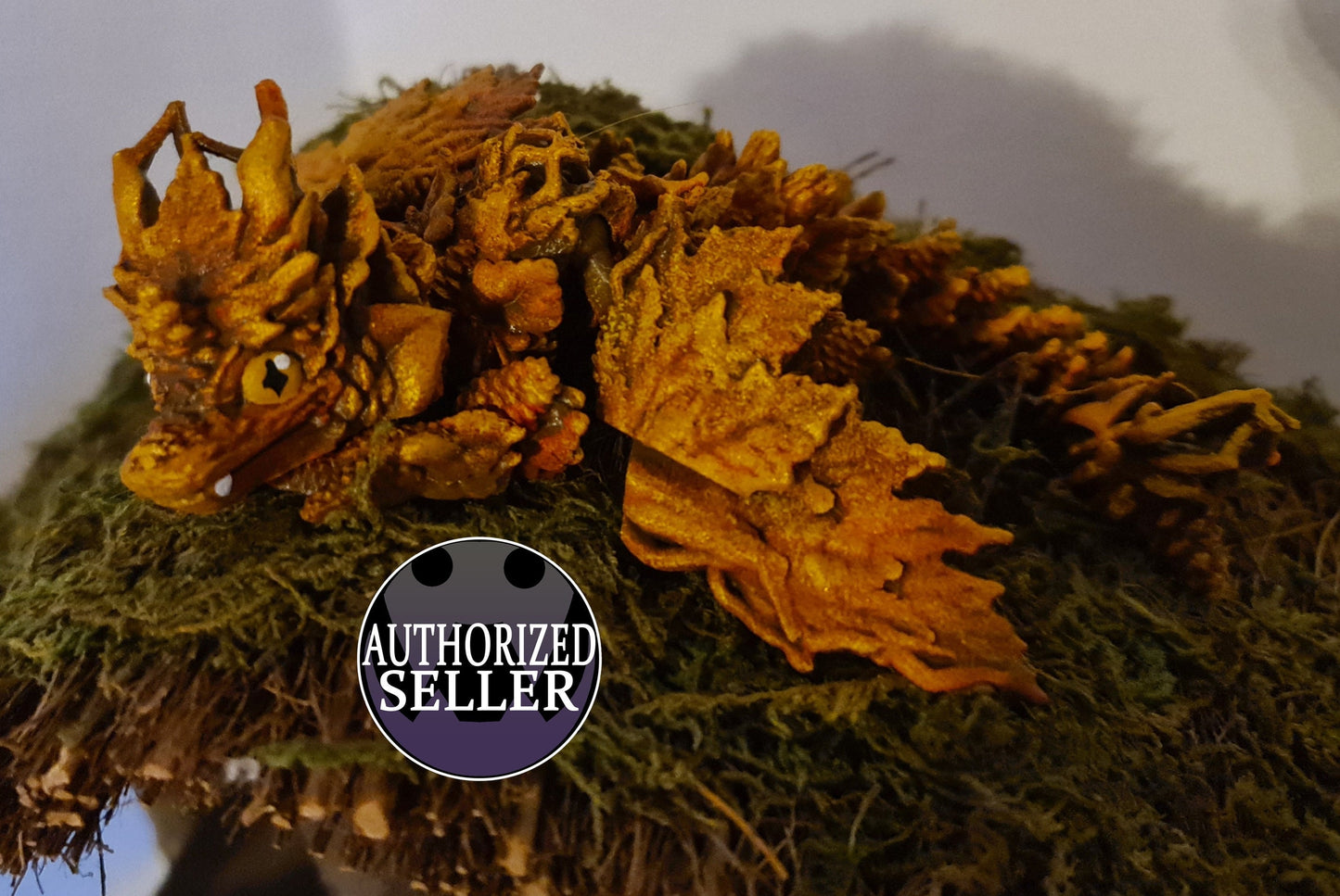 Handcrafted orange dragon figurine with leaf-like wings resting on moss, authorized seller badge