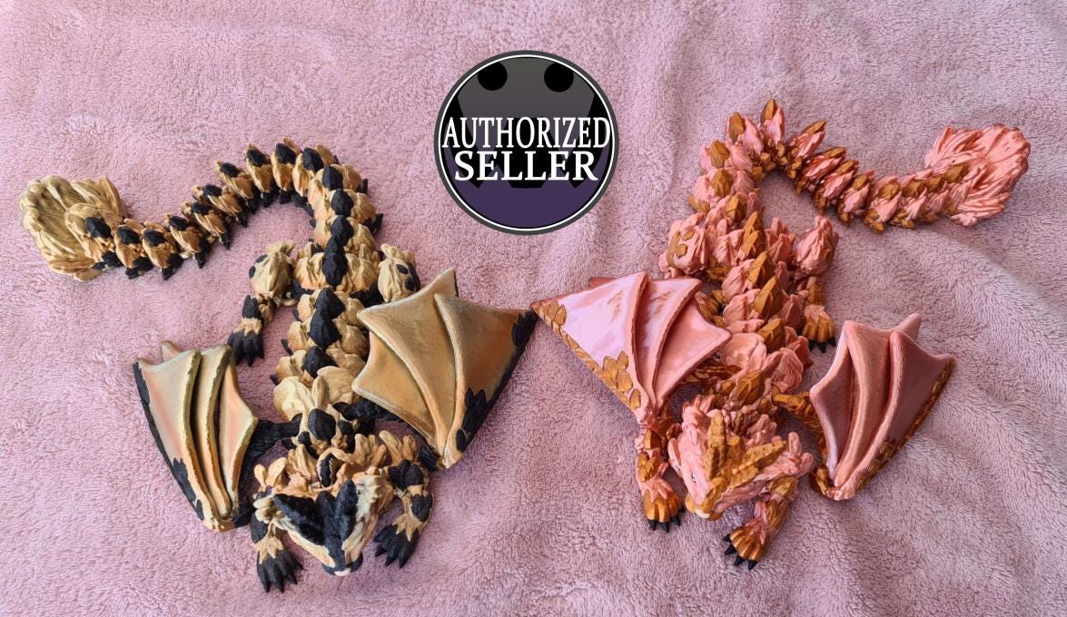 Two articulated dragon figurines, gold and pink, on pink fabric with 'Authorized Seller' badge.