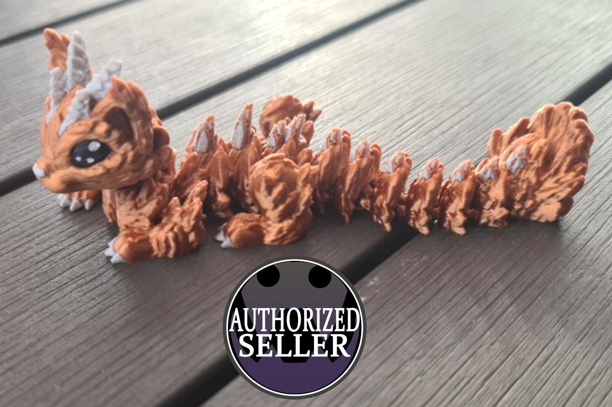 Orange 3D printed dragon figurine with white horns and claws on a wooden surface, authorized seller badge